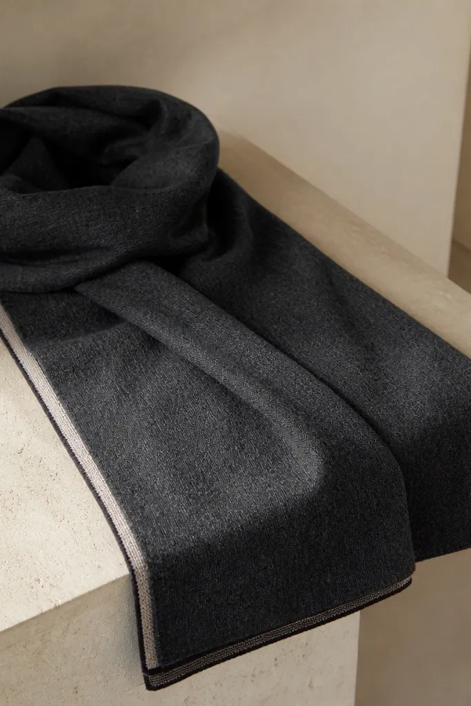 A charcoal gray scarf with a subtle brushed texture and a very thin stripe along one edge, folded once so the stripe forms a neat border. The fabric looks soft and dense with no visible fuzz.