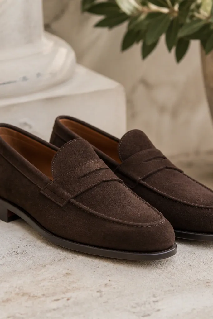 Dark brown suede loafers with a clean moc toe line and a leather sole. The suede has a soft nap and looks well-finished with no obvious wear.