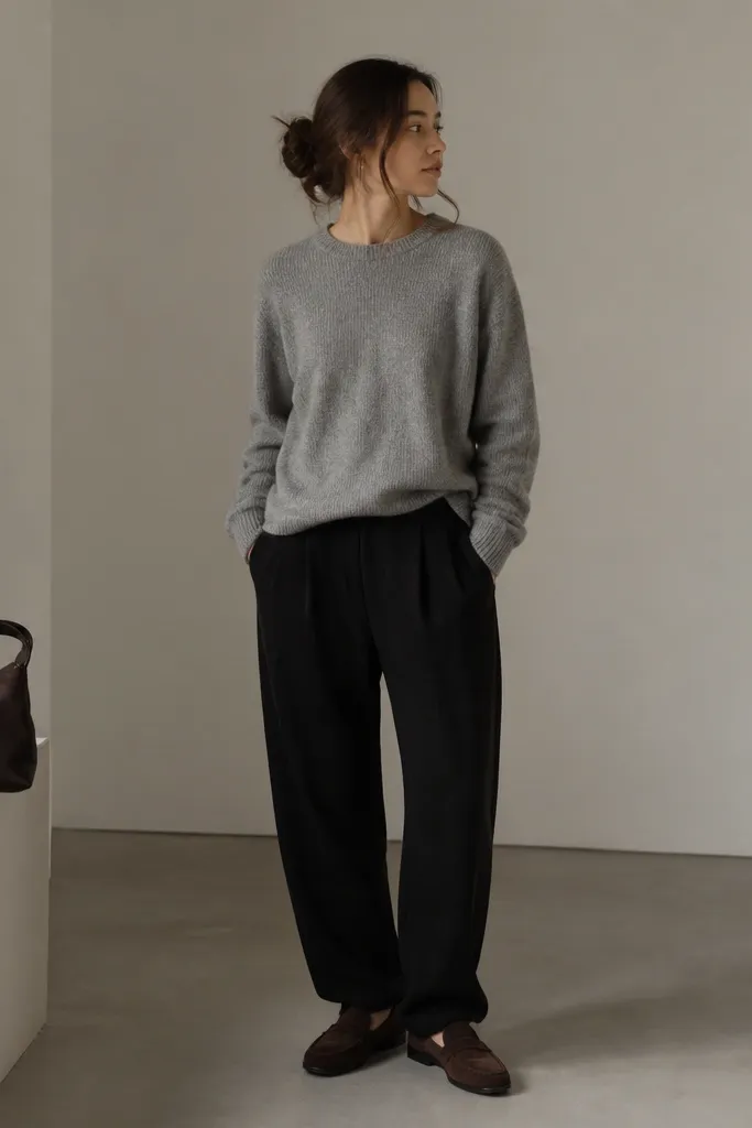 Photo shows black linen pants, a heather gray marl crewneck sweater worn slightly loose, and chocolate suede loafers. A small leather bag in dark brown sits on the side.