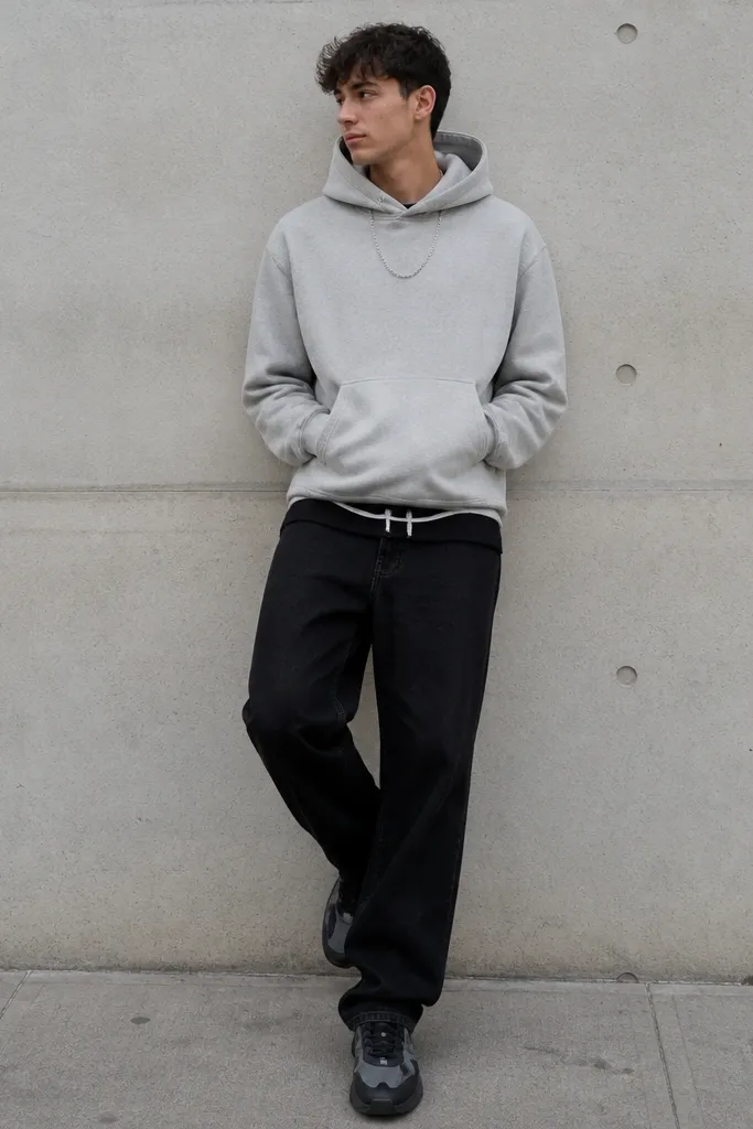 A gray hoodie worn with black jeans. The person shows a small amount of track shorts hem at the waistband area, plus a silver chain. Shoes are black and gray sneakers.