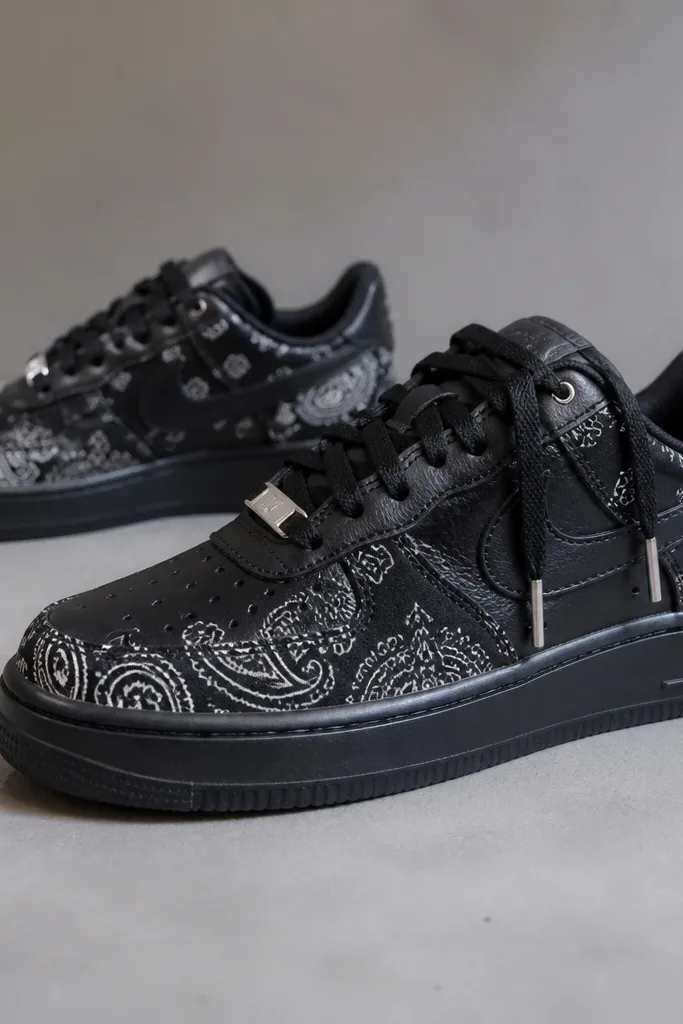 Sneakers with black bandana print, black leather base, and small metallic silver lace tips and hardware details; dark sole with subtle sheen.