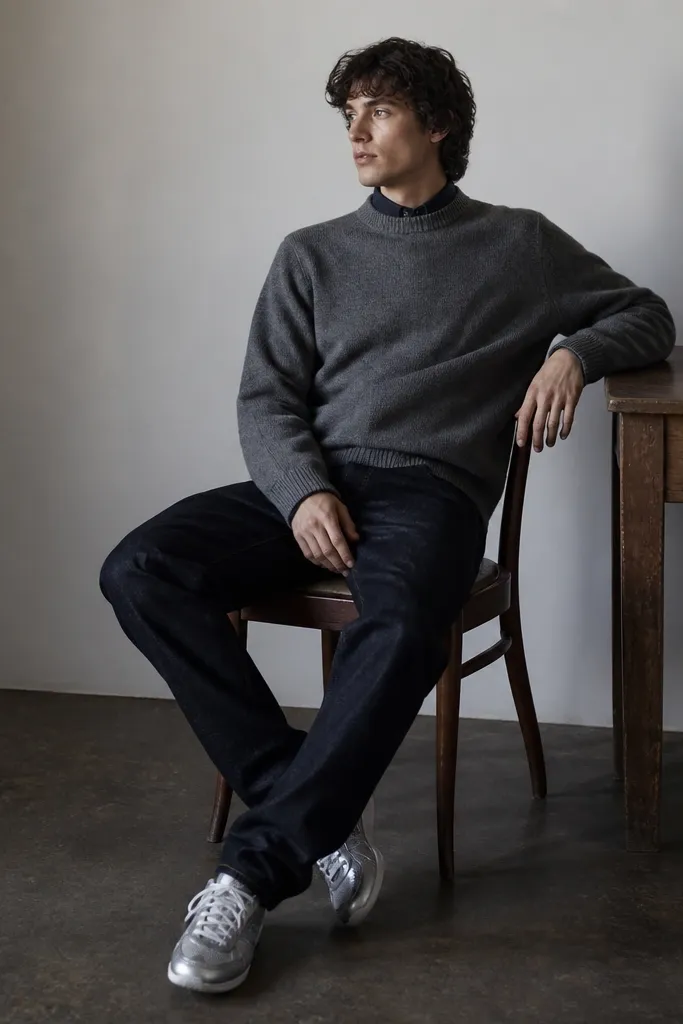 A steel gray knit crewneck sweater with a slightly loose fit over a dark indigo button-up collar peeking at the neckline. Dark wash denim jeans complete the look. Silver Onitsuka Tiger sneakers are centered with laces tied neatly.