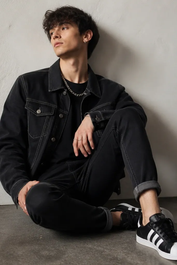 A black denim jacket with contrast stitching over a black t-shirt, black skinny jeans with rolled cuffs, black and white Superstar sneakers, and a chunky silver chain necklace.